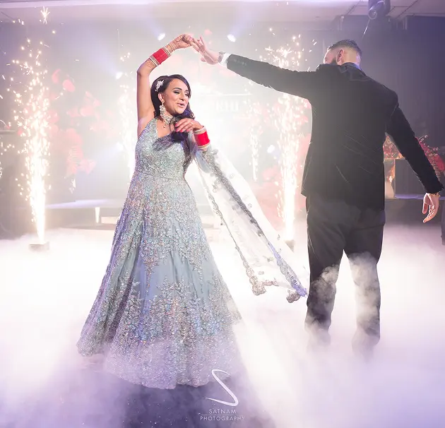 Elegant couple dancing at a glamorous wedding with sparkling lights and smoke effects on the dance floor.