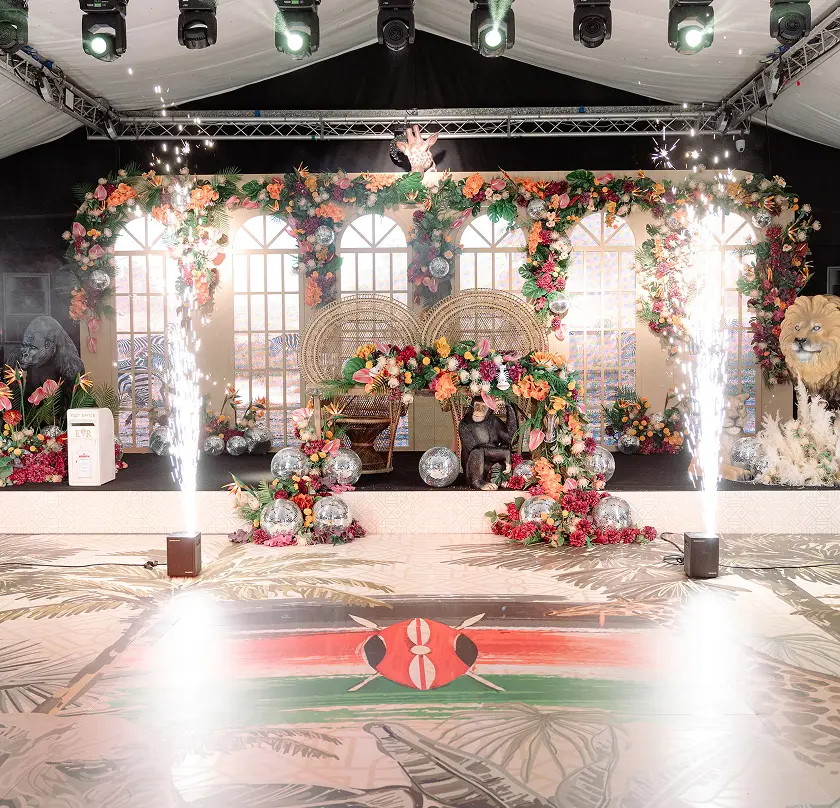 Vibrant wedding stage with floral decor, rattan chairs, and Kenyan flag theme.