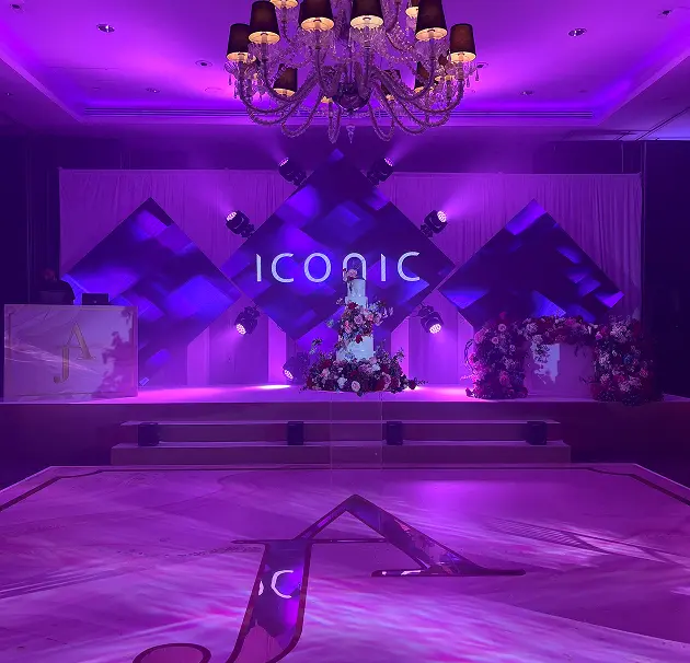 Elegant event stage design with purple lighting and floral arrangements. Iconic sign illuminated in the background.