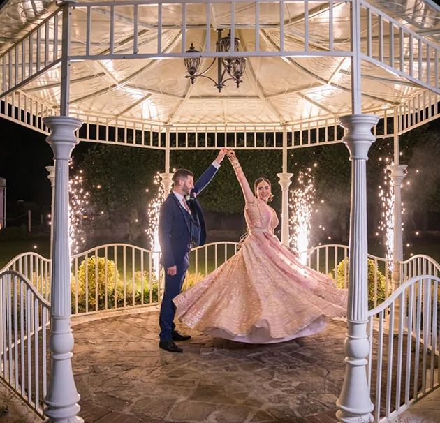 Couple dancing under a gazebo with fireworks in the background, creating a magical night wedding scene.