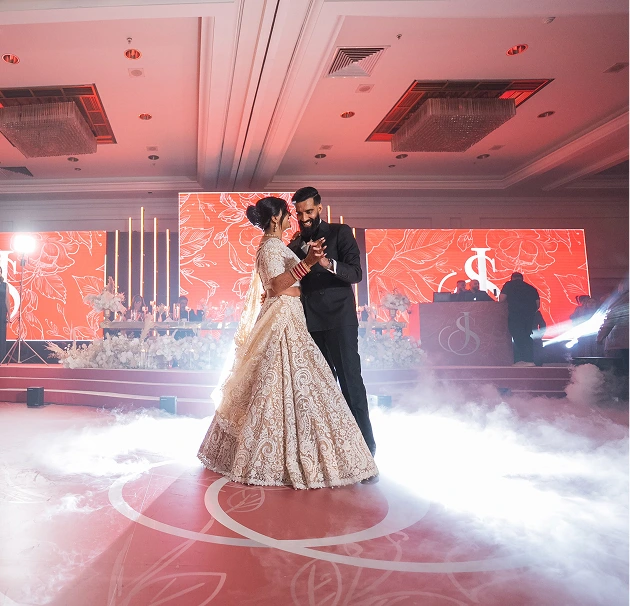 Bride and groom share a romantic first dance on a smoke-filled wedding reception floor with elegant decor.