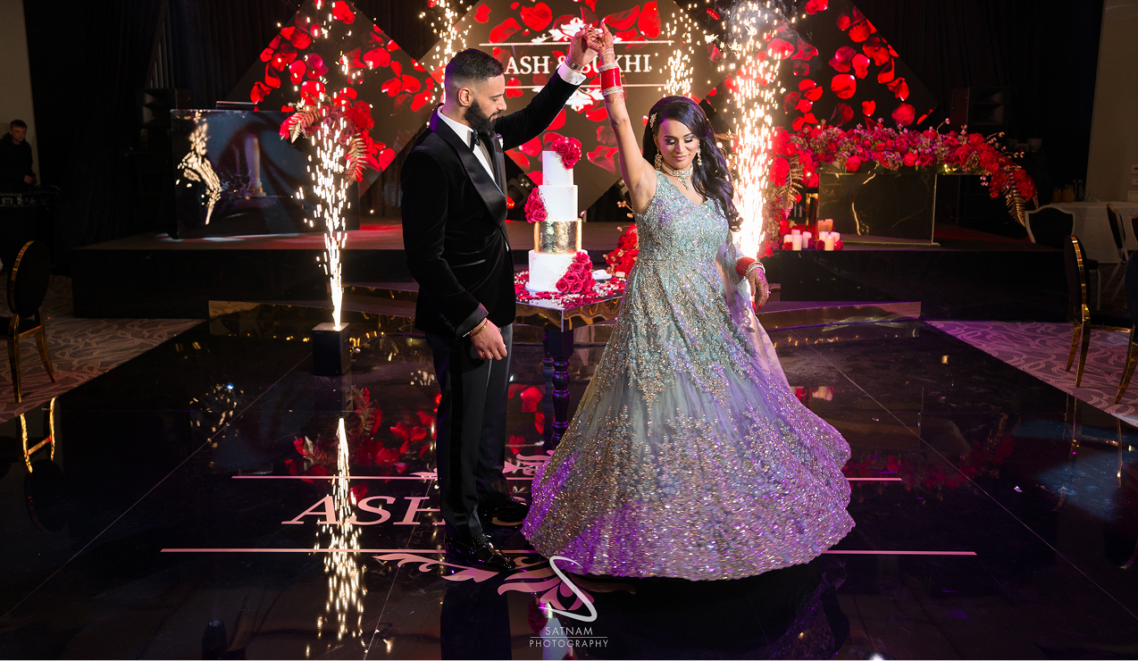Elegant couple dancing at a beautifully decorated wedding reception with lights and roses in the background.